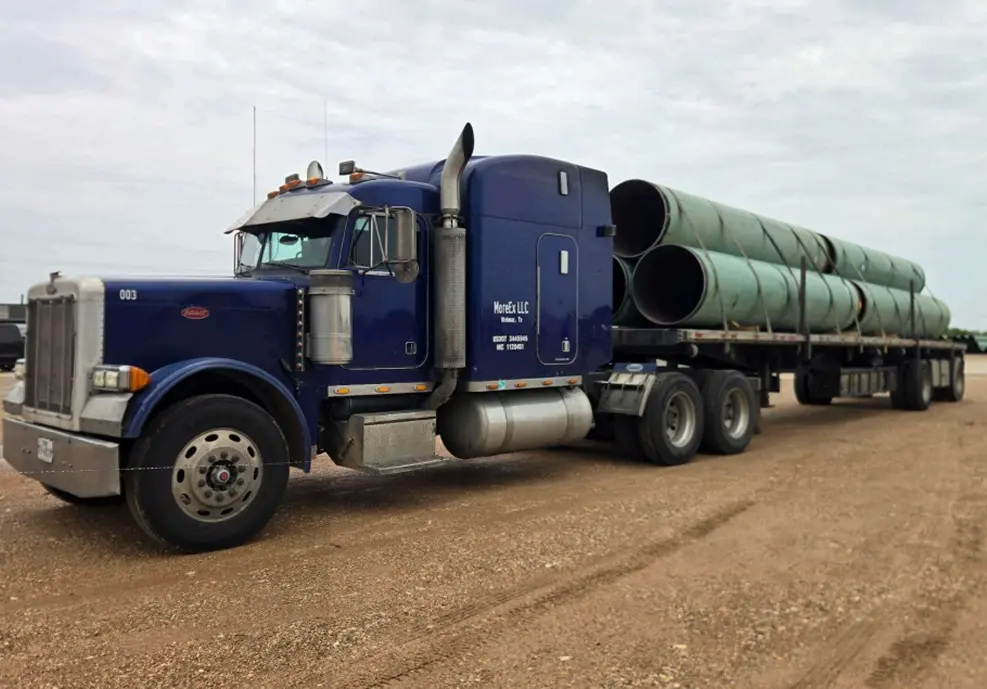 Blue truck hauling large green pipes